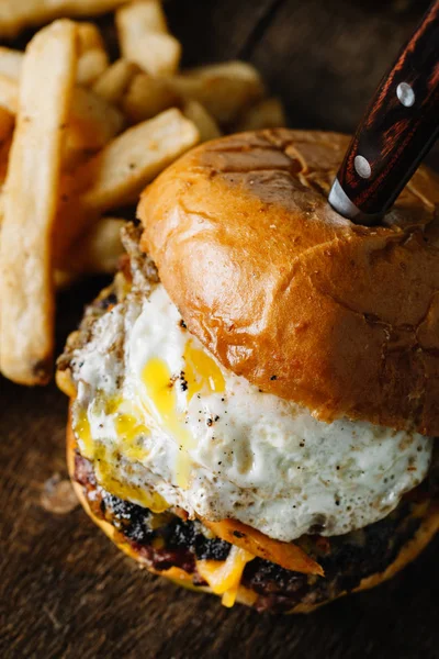 Hamburger da colazione con uovo fritto su superficie rustica scura — Foto Stock