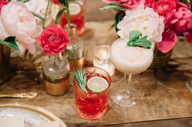 Beyaz ve pembe insanlar, cıva cam vazolar ve mumlarla süslenmiş bir düğün masasında iki imzalı kokteyl.