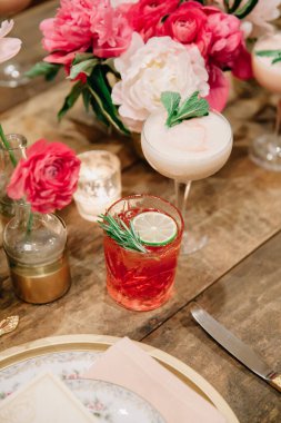 Beyaz ve pembe insanlar, cıva cam vazolar ve mumlarla süslenmiş bir düğün masasında iki imzalı kokteyl.