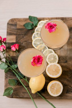 Ahşap bir yüzeyde yenilebilir çiçeklerle süslenmiş iki kokteyl.