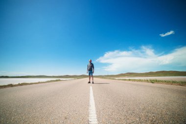 bir adam bozkırda bir asfalt yolun ortasında duruyor