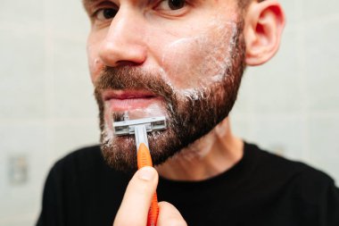 Traş köpüğü ve havluyla jilete homurdanan bir adam.