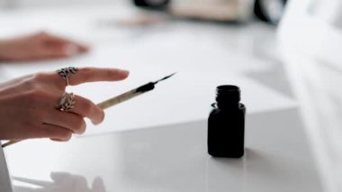 Woman holding a pen for calligraphy in her hands and soaking in an inkwell