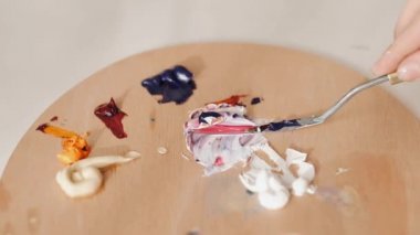 Woman hand mixing oil paints on wooden palette.