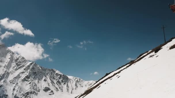 Спускается красный подъемник на фоне снежных гор — стоковое видео