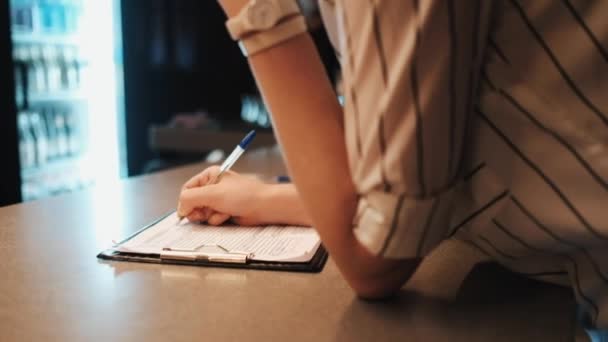 Chica toma un pedido por teléfono y escribe en un cuaderno en un café oscuro — Vídeo de stock