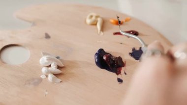 Woman hand mixing oil paints on wooden palette.