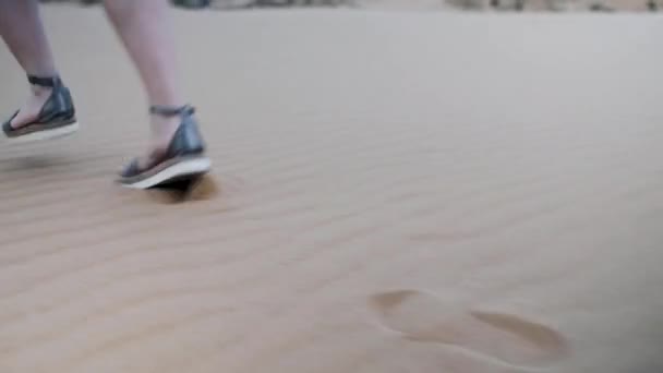 Una donna corre a piedi nudi su una spiaggia di sabbia al rallentatore in sandali . — Video Stock