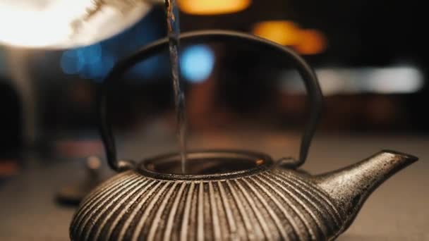 Pouring hot water into a cast-iron kettle, bathed in artificial light in a cafe — 图库视频影像