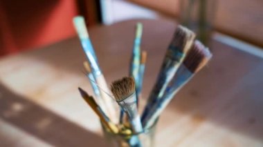 A brush in a glass on a background of a red wall backlit by the rays of the sun.
