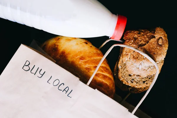 Compra local. leite e pão em uma mesa preta com um saco de artesanato — Fotografia de Stock