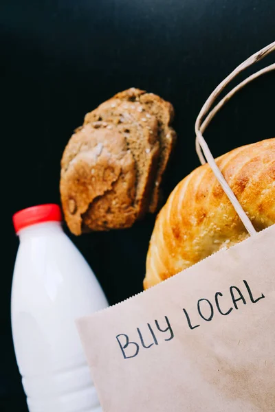 Compra local. leite e pão em uma mesa preta com um saco de artesanato — Fotografia de Stock