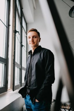 Gülümseyen yakışıklı bir iş adamı, pencerenin yanında duruyor. 