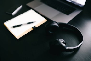 Kayıt defteri, dizüstü bilgisayarı ve kulaklığı olan karanlık modern bir işyeri. 