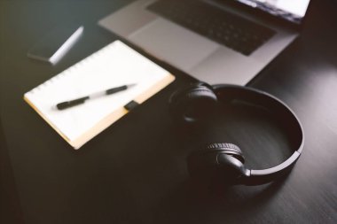 Kayıt defteri, dizüstü bilgisayarı ve kulaklığı olan karanlık modern bir işyeri. 