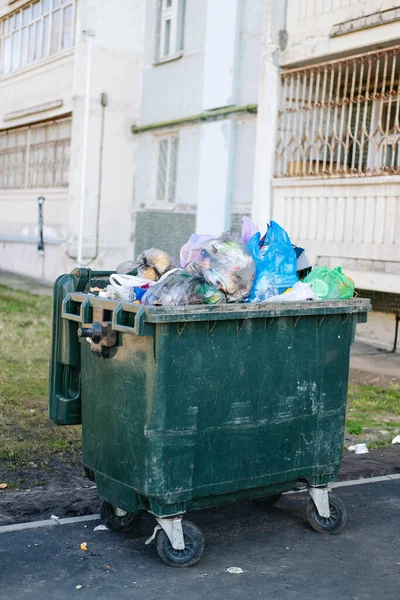 Bidone della spazzatura completo sullo sfondo di una casa prefabbricata Foto Stock