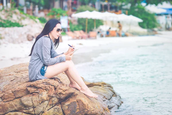 Frau schreibt am Strand mit Stift auf Notizblock. — Stockfoto