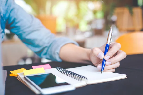 Mujer mano está escribiendo en el bloc de notas con un bolígrafo en la oficina . — Foto de Stock