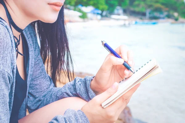 Woman writing on notepad with a pen at the beach. Stock Image