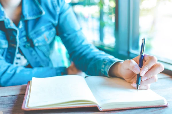 Mulher mão está escrevendo em um bloco de notas com uma caneta no escritório . — Fotografia de Stock