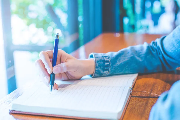 Mujer mano está escribiendo en un bloc de notas con un bolígrafo en la oficina . — Foto de Stock