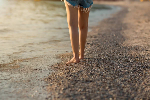 Beine von Frauen, die bei Sonnenuntergang am Strand spazieren. — Stockfoto