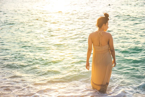 Mujer en vestidos de crema observa la hermosa puesta de sol en la playa — Foto de Stock