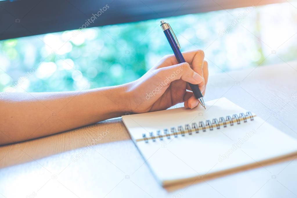 Woman hand is writing on a note pad with a pen.