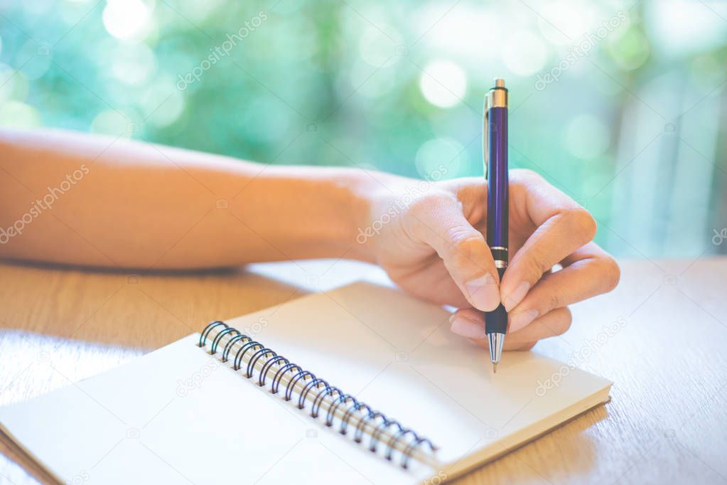 Business woman hand is writing on a note pad with a pen in offic