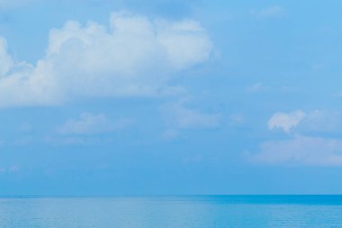 Yüzen bulutlar, mavi gökyüzüne ve denize karşı yumuşak renkler.