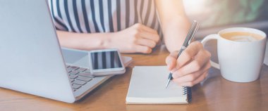 İş kadını bilgisayarda çalışıyor ve not defterine yazı yazıyor.