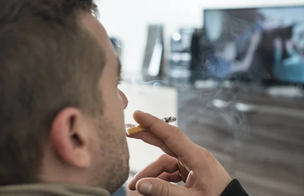 Mannen røyker en sigarett i huset. . – stockfoto