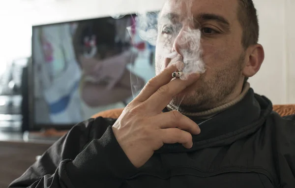 Ο άνθρωπος καπνίζει ένα τσιγάρο στο σπίτι. — Φωτογραφία Αρχείου