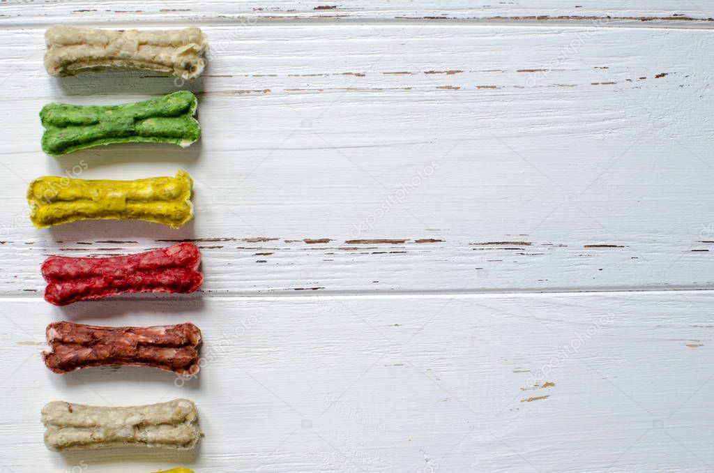 Delicious chewing colored bones for dogs with different tastes on white wooden background