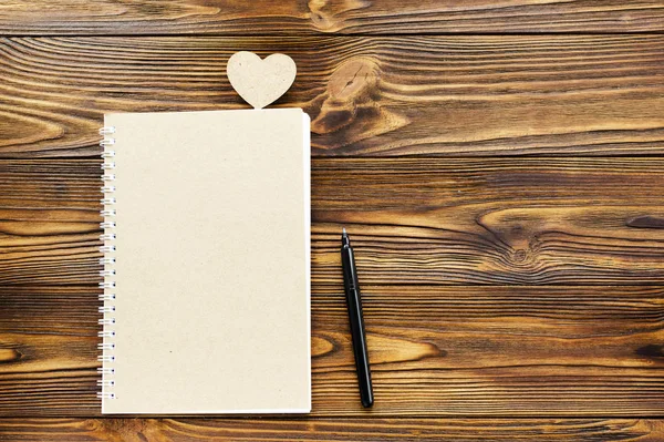 Kraft papier blocnote, pen. houten hart op houten achtergrond en — Stockfoto
