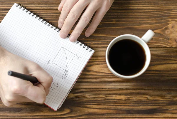 Mani di uomini che scrivono in blocco note e tazza di caffè su ta di legno — Foto Stock