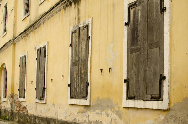 Wall of old building with window with  closed wooden shutters