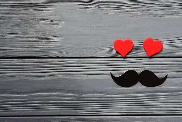 paper mustache and red hearts on grey wooden background