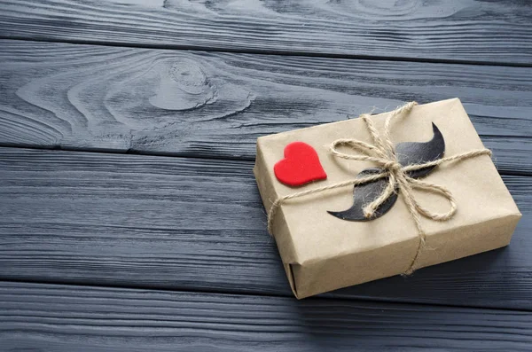Boîte cadeau enveloppée dans du papier kraft avec moustache en papier et ouïe rouge Images De Stock Libres De Droits