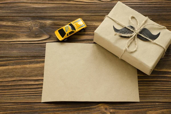 Gift box wrapped in kraft paper with paper mustache on brown woo — Stock Photo, Image