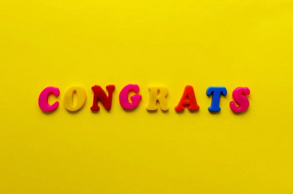Λέξη «συγχαρητήρια» από μαγνητικά γράμματα σε φόντο κίτρινο χαρτί — Φωτογραφία Αρχείου