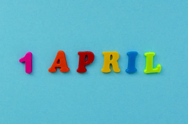 Färgglada text ' 1 april ”av magnetiska bokstäver på blått papper tillbaka — Stockfoto