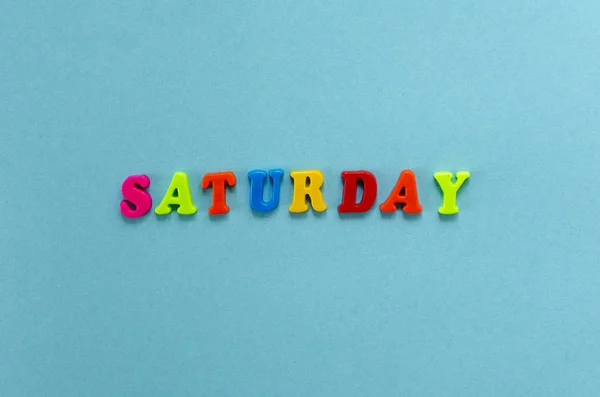 Word "saturday" of colored plastic magnetic letters on blue pape — Stock Photo, Image