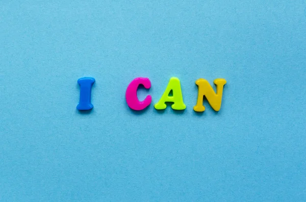 Frase "i can" of colored plastic magnetic letters on blue paper Stok Gambar