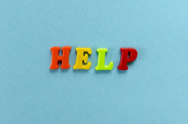 Mot "aide" de lettres magnétiques en plastique coloré sur papier bleu ba Image En Vente
