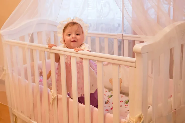 Baby flicka stående i sin spjälsäng. — Stockfoto