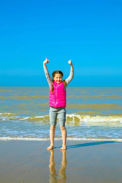 Little girl showing thumbs up on the shore — Stock Photo, Image