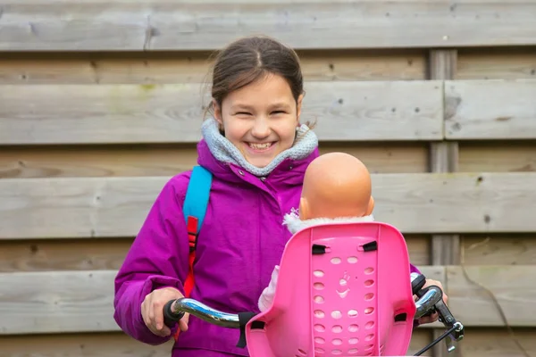 Девушка на велосипеде с куклой. Ребенок едет на велосипеде — стоковое фото