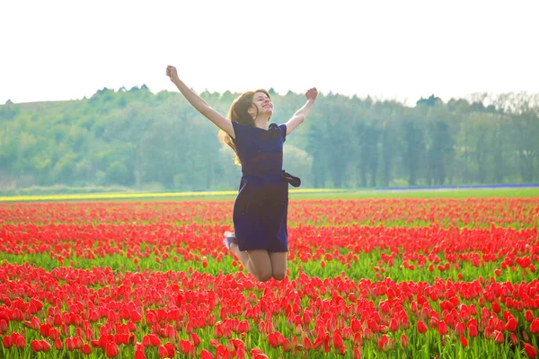 Šťastná mladá dospívající dívka skákání proti jarní Tulipán pole. — Stock fotografie