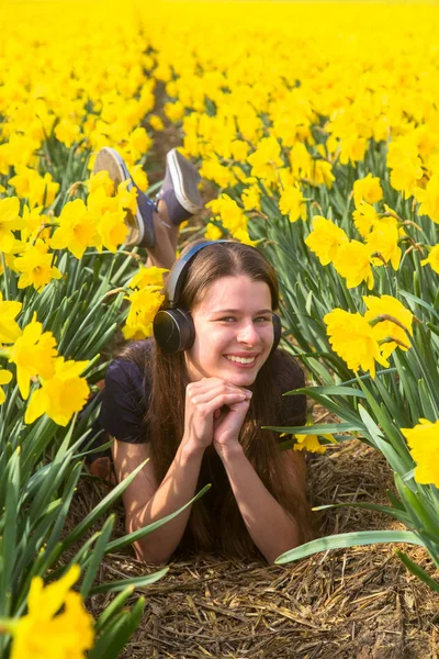 Dospívající dívka poslechu hudby ve sluchátkách v květiny — Stock fotografie